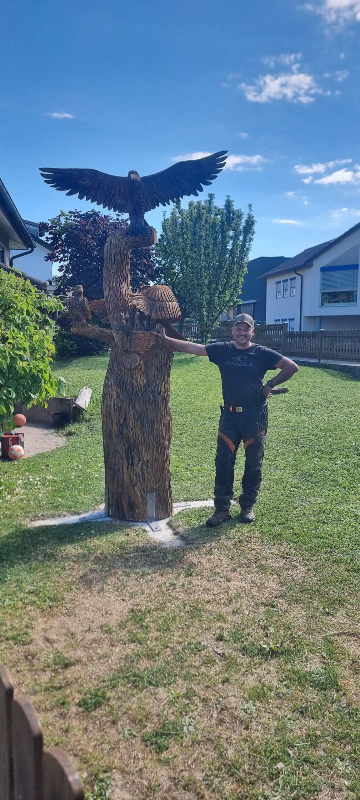 Chris Beyer neben einer großen Holzskulptur mit Adler